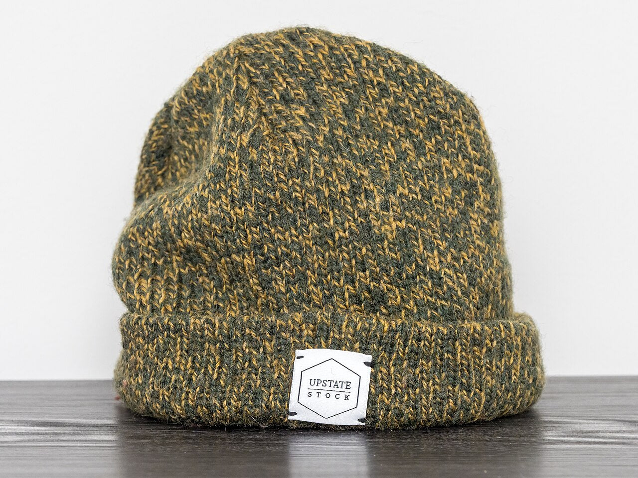 Green and gold marled ribbed knit beanie with a folded cuff, standing on a dark wood surface