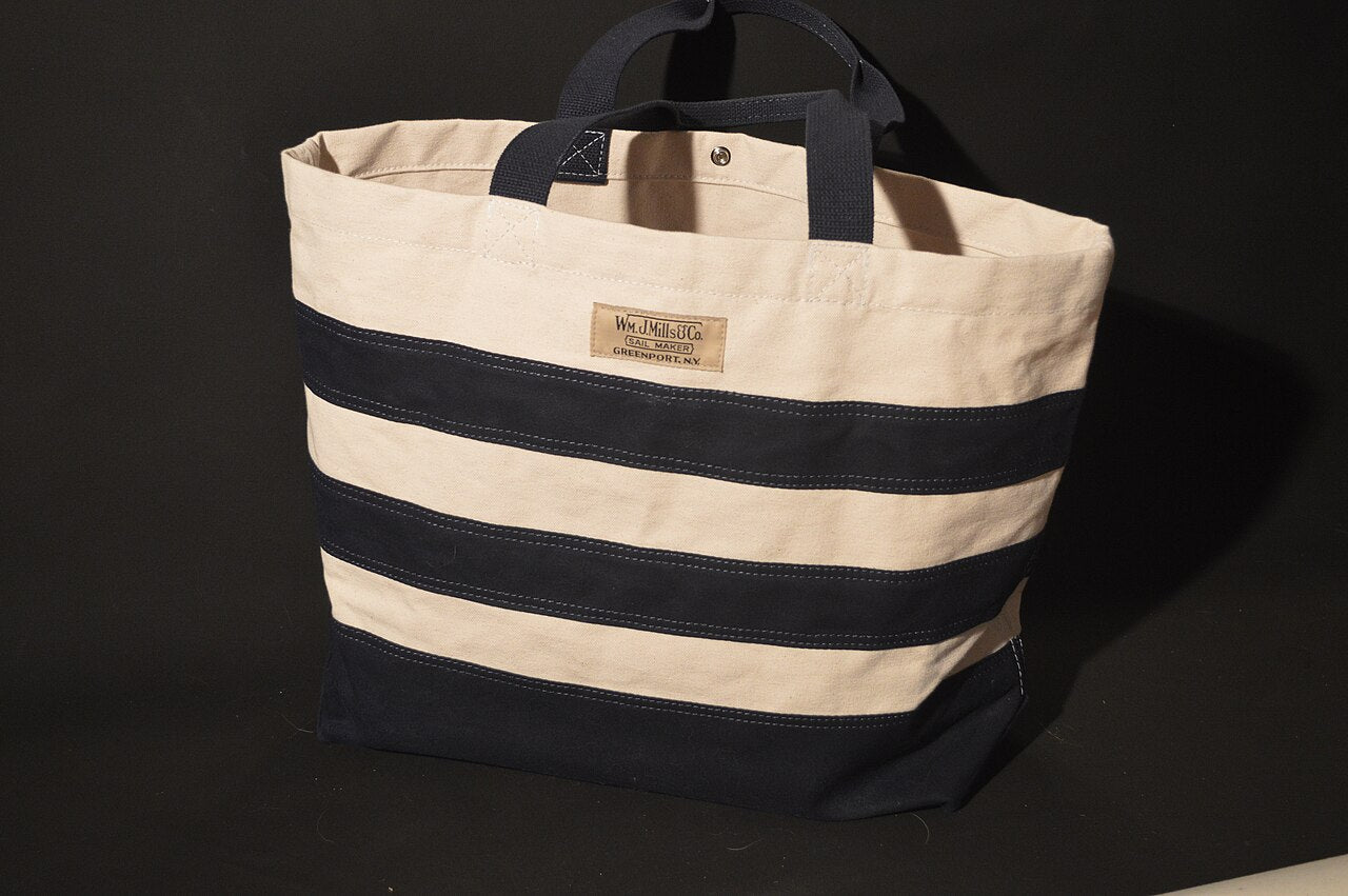 Natural canvas tote bag with navy horizontal stripes and navy webbing handles on a black background