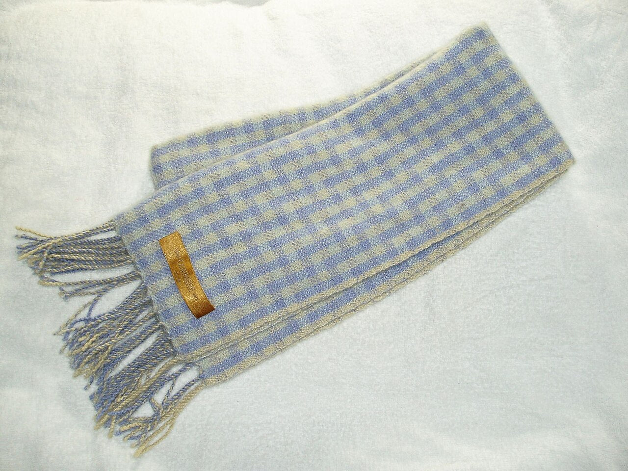 Folded pale blue and cream checked woollen scarf with knotted fringe on a white surface