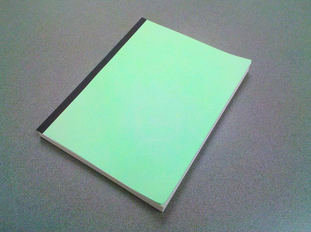 A slim paperback book with a plain mint green cover and black spine lying on a grey desk