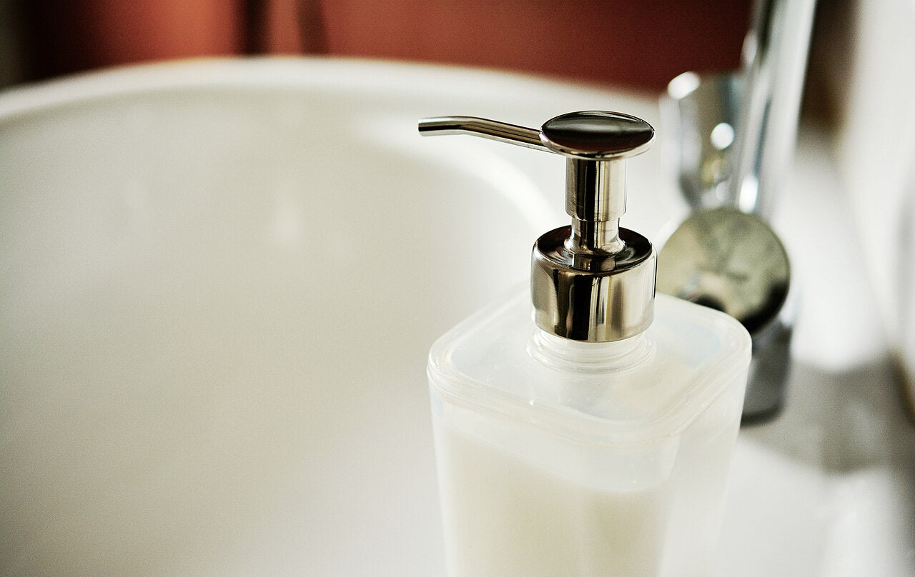 Frosted pump bottle of white liquid soap with a chrome pump head beside a basin