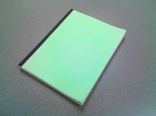 A slim paperback book with a plain mint green cover and black spine lying on a grey desk