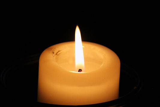 Lit cream pillar candle with a single flame, close up against a black background