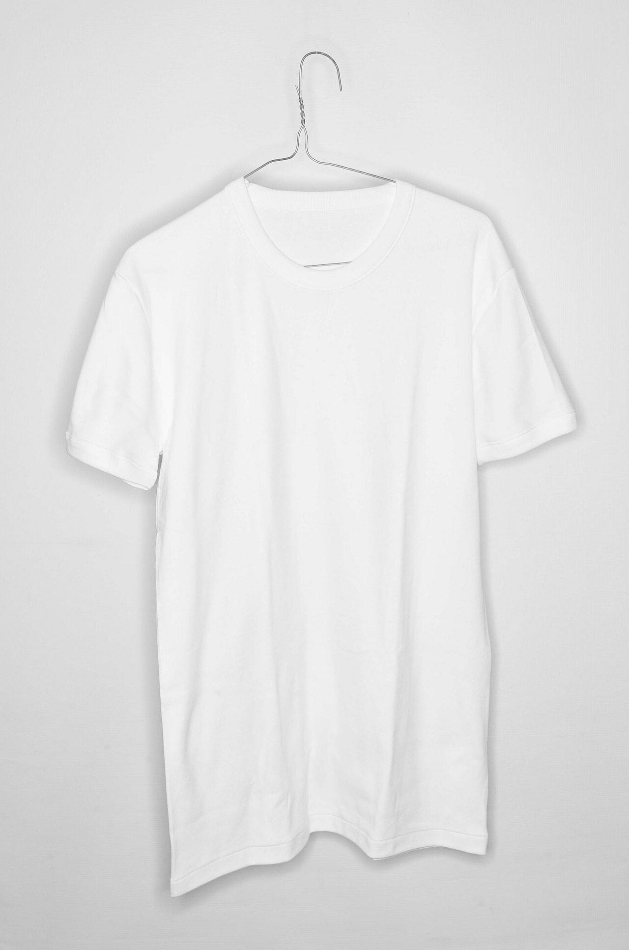 Plain white short-sleeved t-shirt hanging on a thin wire hanger against a pale grey wall