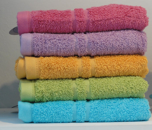 Stack of five folded terry towels in pink, lilac, yellow, green and turquoise against a plain wall