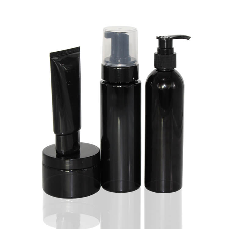 Four unlabelled glossy black cosmetic containers, a squeeze tube, foam pump, lotion pump and jar, on white