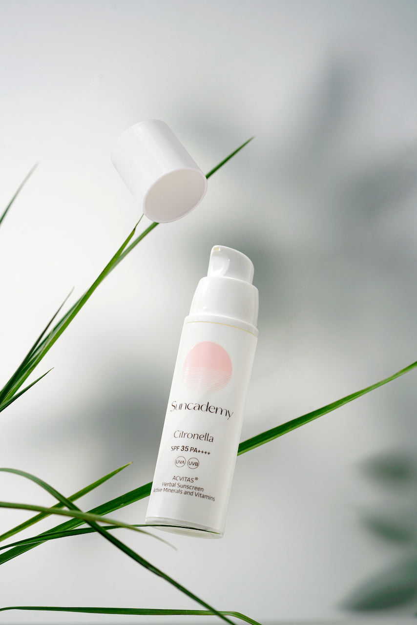 White pump bottle of sunscreen with the cap floating off, shot against a pale background among green grass blades